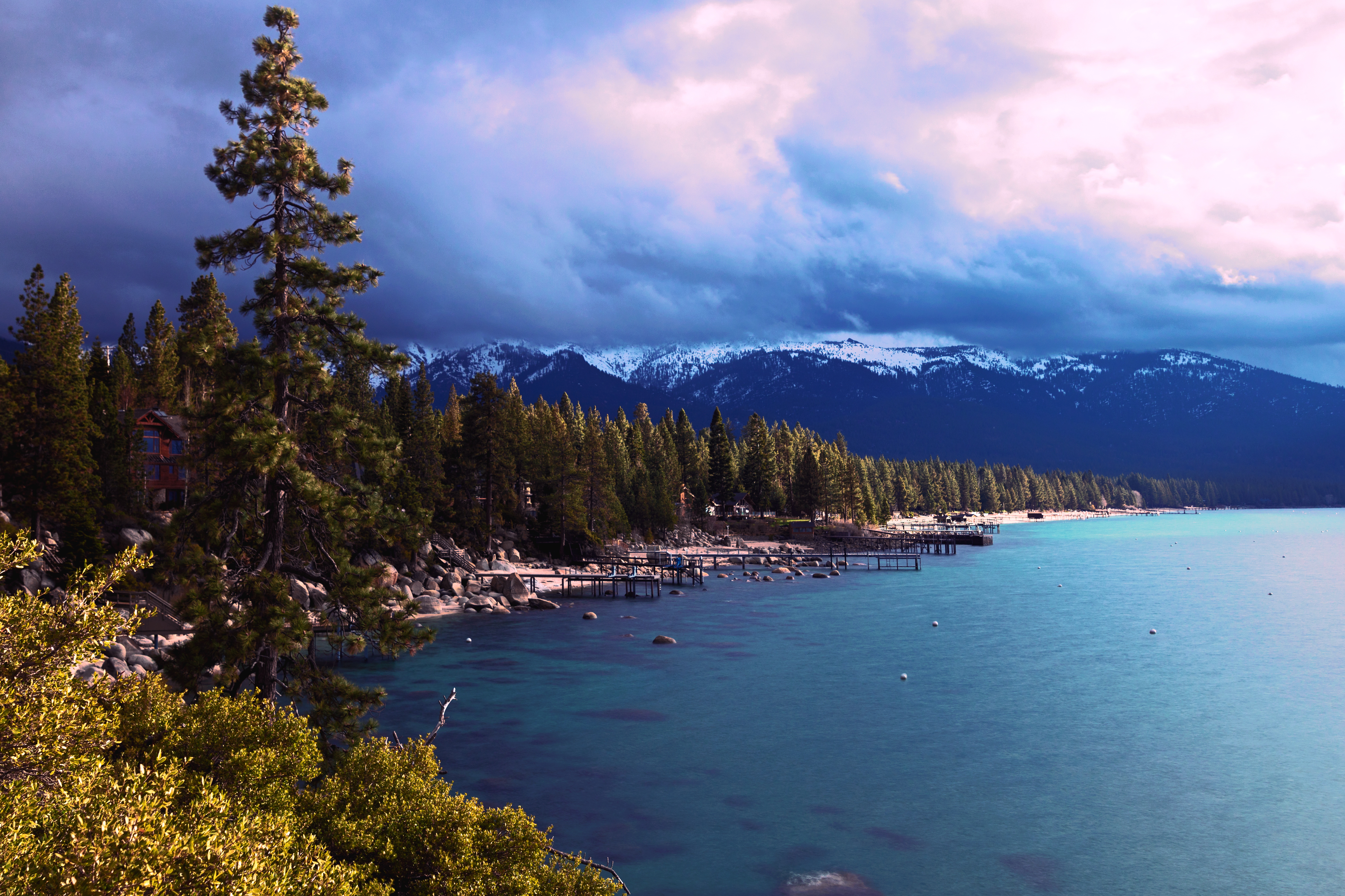 Turquoise lake Tahoe shoreline with piers reaching into the water and a dramatic cloudy backdrop.