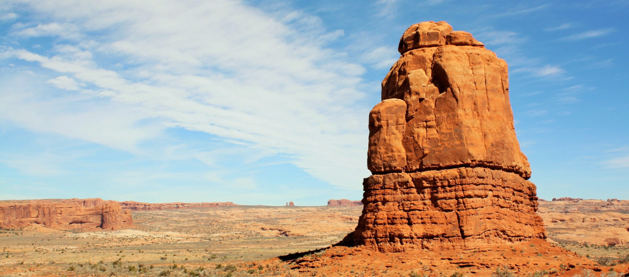 Arches National Park - Monument Valley like sanstone pillar surrounded by blue sky and open terrain.